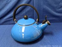 Front angle showing the blue enamel kettle with black handle and lid knob, spout cover closed.