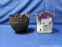 Photo showing front and side views of two cityscape ceramic vases on a blue fabric background.