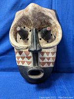 Front view of Bakuba mask showing protruding nose cones, geometric red triangle patterns, open mouth, and eye holes with surrounding small holes.