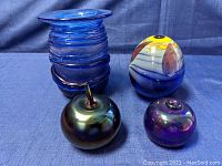 Four signed art glass pieces placed together on a blue cloth background illuminated by natural light, showing various shapes and colors.