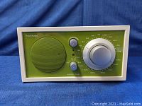 Front view of the Tivoli Audio Model One radio showing the green front panel, speaker grille, volume and tuning knobs, and frequency markings.