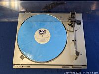 Top view of the Technics Auto SL-BD2 turntable with blue PAT Travers vinyl record on platter and dust cover closed.