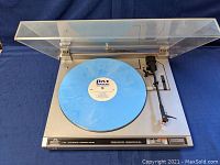 Full top view of JVC L-A110 turntable with blue vinyl record, clear plastic dust cover open.