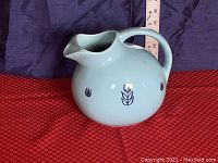 Blue vintage ceramic ball pitcher with tulip and leaf motif, bulbous shape, open-loop handle, and curved pouring spout.