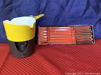 Yellow enameled cast iron fondue pot with black cast iron tea light stand and six fondue forks in original box