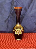 Front view of tall amethyst glass vase with floral enamel decoration and gold accents, showing vase shape and design.