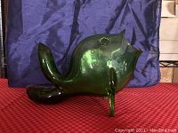 Side view of green Empoli glass fish sculpture showing body, back fin, rear, and three legs supporting the fish, with visible reflection and light distortion on surface.