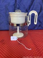 Front view of vintage Gemco glass stove top coffee percolator on red surface with blue backdrop.