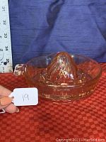 Front angled view of the pink Depression glass citrus juice reamer showing the side tab handle and ridged reaming cone. Scale in the background for size reference.