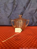 Front view of the pink depression glass sugar bowl with two handles and lid showing the cherry blossom pattern engraved on side panels.