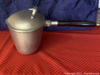 Side view of triangle-shaped cast aluminum pot with long black handle and lid on.