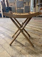Side angle of mid-century folding slat wooden stool showing crossed legs and curved slat seat.