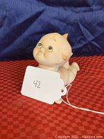 Bisque porcelain Kewpie doll figurine lying crawling side view on red checkered surface, showing doll's posture and details