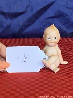 Front view of the bisque porcelain Kewpie doll showing seated baby with sad expression and hand positioning