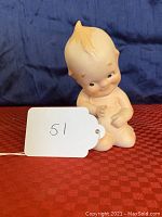 Small bisque porcelain Kewpie doll figurine photographed from the front showing the doll seated with hands in front and distinctive facial features.