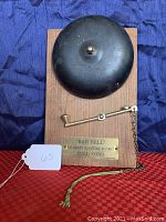Front view of boxing style bar bell mounted on wooden plaque with brass pull arm and green braided cord. Shows engraved plate instructions and overall condition.