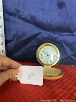 Gold-tone Seth Thomas portable alarm clock closed and shown with scale for size comparison.