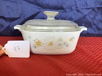 Front view of vintage Corning Ware 1.5qt casserole dish with floral bouquet pattern, white ceramic with colorful flowers and glass lid.