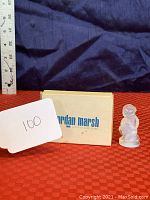 Photo showing the Sabino signed cherub figurine next to a ruler and Jordan Marsh box on red surface.