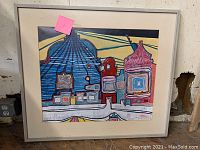Framed abstract artwork with colorful architectural forms and signature visible in lower left corner.