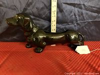 Side view of the black porcelain dachshund planter with a measuring tape showing length and height, standing on a red surface with a black background.