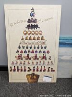 Front view of an Ann Geddes lithograph showing The Twelve Days of Christmas figures arranged in tiers on a beige board