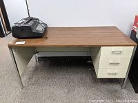 Full image of the metal framed desk with woodgrain top and three drawers on the right side. Shows overall size and condition.