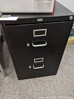 Front view of the black filing cabinet showing two drawers with silver handles and label holders, with visible keyholes on each drawer.