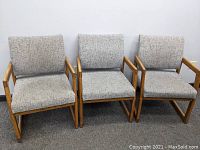 Front view of three grey upholstered chairs with wooden frames showing seat cushions, back cushions and armrests.