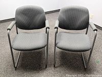 Front view of two grey fabric occasional office chairs with metal frames and armrests.