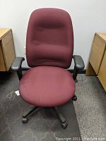 Front view of the maroon office chair showing the cushioned seat, backrest, and worn black arm pads.