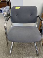 Front view of grey occasional chair showing cushioned seat and backrest with chrome frame and black arm pads.