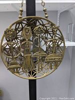 Front view of brass wall hanging showing four stylized female figures in a circular geometric design.