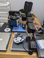 Photo of the three boxes containing assorted laptops, audio equipment like Sony speakers, cables, and other electronic devices on a wooden table.