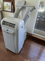 Front and top view of white portable unit with hoses attached; window adapter panel behind