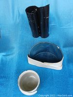 Photo showing the three Patricia signed pottery pieces: tall double black vase on top, oblong cream and blue planter below, and round cream and blue small vase in front on a blue cloth background.
