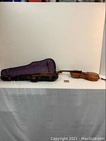Violin, case, and label arranged side by side, showing full length of violin and closed case