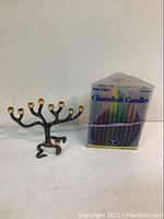 Photo showing metal Tree of Life menorah with gold-colored candle holders beside a box of multicolored Chanukah candles.