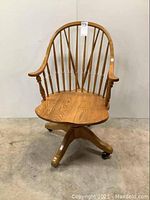 Front view of the oak desk chair showing spindle back, curved armrests, and wooden seat with visible wood grain.
