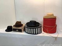Four hats and four hat boxes displayed on table, showing variety of styles and colors including black, beige and red boxes