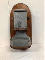 Front view of entire holy water font and receptacle mounted on wooden plaque.