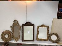 Five ornate mirrors arranged side by side showing various sizes and styles including round and rectangular frames.