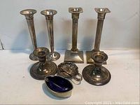 Eleven-piece set displayed, showing four tall candlesticks, two shorter candlesticks, and three salt cellars including blue glass lined and shell-shaped pieces.