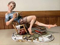 Front view of porcelain boy sculpture showing the boy sitting on a chair reading a book with the signature Merli on the base.
