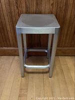Full frontal view of the aluminum stool showing its rectangular legs and footrest support.