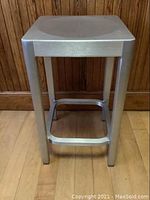 Overall view of the aluminum stool showing its full height, legs, and seat design.