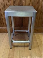 Front view of aluminum stool showing legs and seat, with visible 'Emeco by Starck' stamp.