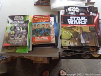 Stack of Star Wars books including story novels, coloring books, and activity books on table surface.