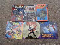 Six Batman themed books arranged on the ground showing covers with Batman characters and titles.