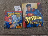 Photo displaying two Superman hardcover books: 'Superman Mayhem of Metallo vs Batman' and 'Superman The Ultimate Guide to the Man of Steel'. Both are visibly used but intact.